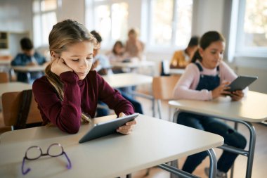 Schoolgirl reading on digital tablet in the classroom at primary school. 