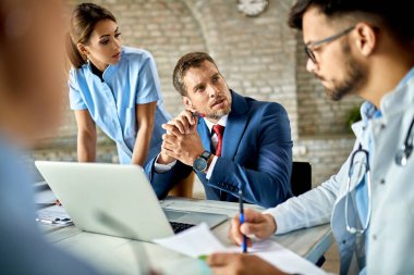 Businessman using laptop while communicating with healthcare workers during the meeting in the office. 