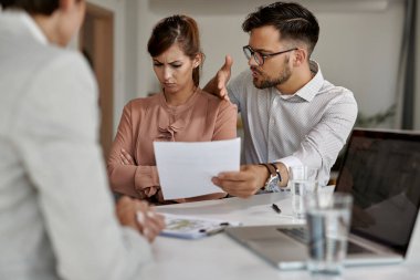 Young man trying to talk with his stubborn wife while analyzing lease agreement on a meeting with real estate agent. 