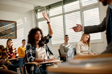 Happy African American female student raising arm to ask a question during lecture at university classroom. 