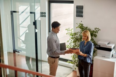 Happy business colleagues going through documents while standing in hallway of an office building. 