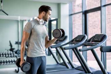 Athletic man working out with dumbbells during strength training in a gym.