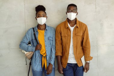 Happy black students with face masks against the wall and college hallway. 