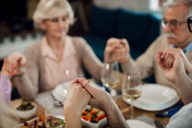 Close-up of multi-generation family holding hands while praying before the lunch at dining table. 