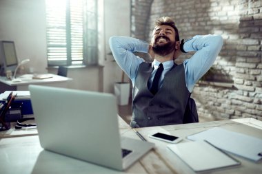 Happy businessman relaxing with hands behind head while taking a break from work in the office. 