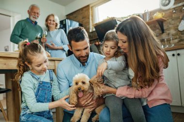 Young parents and their small daughter enjoying with a dog at home. Grandparents are standing in the background. 