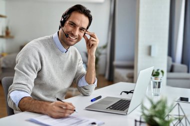 Young happy entrepreneur using laptop and writing reports while working at home. 