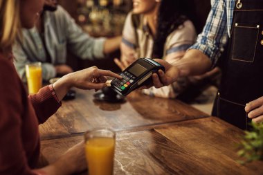 Close-up of female customer paying to a waiter and entering pin on credit card reader. 