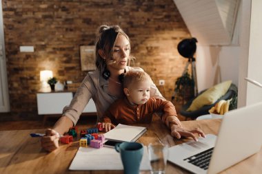 Working mother using computer while small son is sitting on the lap at home. 