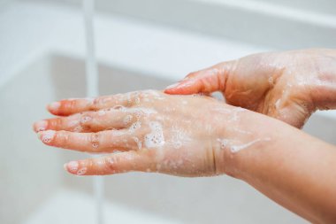 Close-up of woman using soap while hashing hands in the bathroom. 