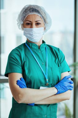 Portrait of confident nurse wearing protective workwear while standing with arms crossed at medical clinic and looking at camera