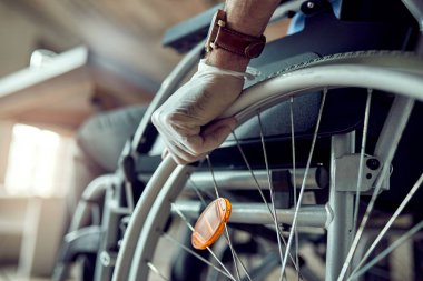 Close-up of disabled businessman wearing protective gloves while pushing himself in a wheelchair. 