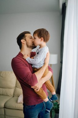Affectionate father holding his son and kissing him at home.