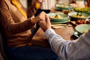 Close-up of people holding hands and praying while sitting at dining table. 