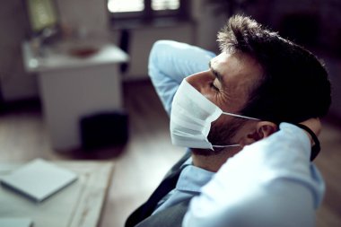 Relaxed businessman with protective face mask taking a break from work in the office.