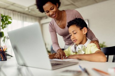 Black boy learning at home while his mother is helping him with the assignment.