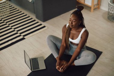 Afrika kökenli Amerikalı atletik kadın, yoga ve meditasyon yaparken dizüstü bilgisayar kullanıyor.. 
