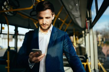 Mid adult businessman using cell phone and reading text message while commuting to work by bus.