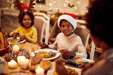Happy black boy talking to his mother and sister during Christmas dinner at dining table.