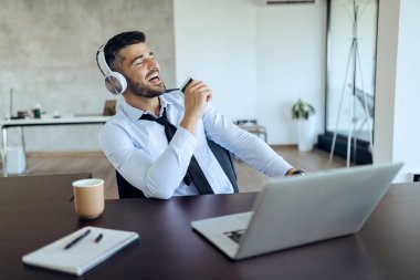 Young entrepreneur having fun and singing while listening music on headphones on a break in the office.