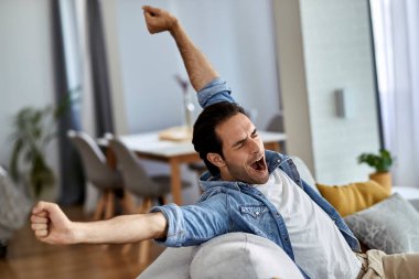 Evdeki kanepede otururken kendini yorgun ve esniyor hisseden genç adam.. 
