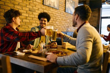 Young happy men toasting with beer while having lunch together in a pub. 