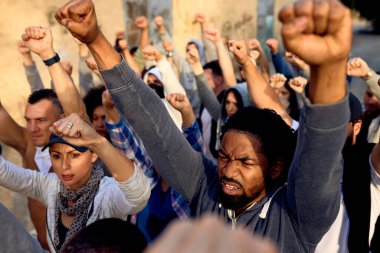 Young black man marching with crowd of people with raised fists on public demonstrations. 