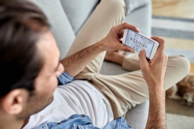 Close-up of a man using mobile phone and signing up for a webinar at home. 
