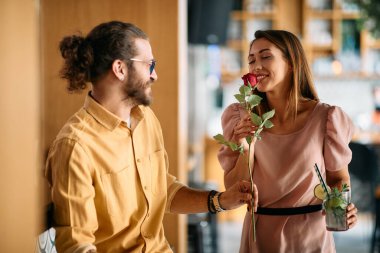 Romantic man giving his girlfriend red rose on their date in a cafe. Focus is on woman smelling the flower. 