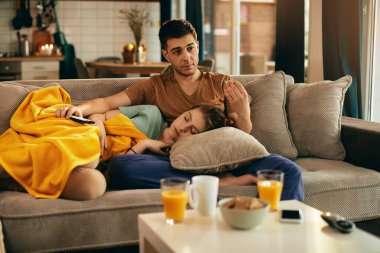 Young woman taking a nap while her boyfriend is watching TV at home. 