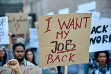 Crowd of unemployed people protesting against loosing their jobs due to coronavirus pandemic. Focus in on banner with I want my job back inscription. 