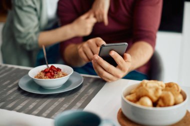Close-up of couple using using smart phone while having breakfast at home.