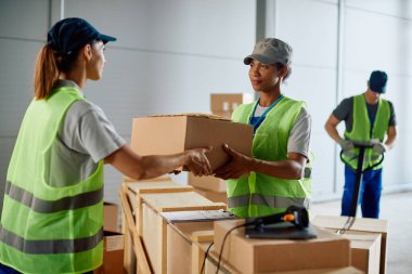 African American warehouse foreman giving to female worker packages for shipment from   storage room.