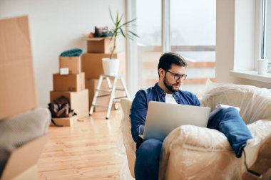 Mid adult man using laptop and going through documents while relaxing on the sofa at his new home. 