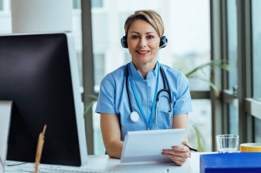 Smiling female doctor wearing headset while working at medical call center and looking at camera.