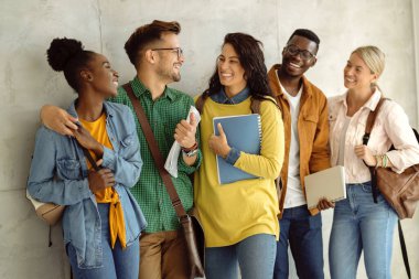 Group of happy university students standing in a hallway and talking to each other. 
