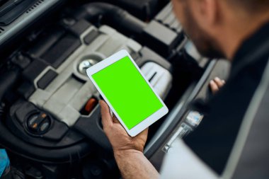 Close-up of auto repairman using touchpad while working at car workshop. Focus is on green touchscreen. Copy space. 