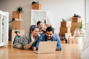 Happy family using laptop and greeting someone after moving into their new home. 
