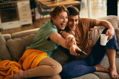 Cheerful woman having fun while watching TV with her boyfriend at home.