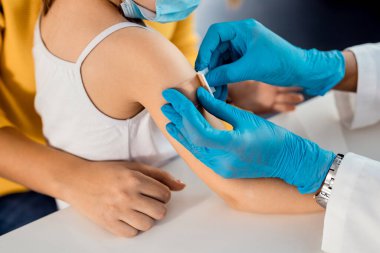 Close-up of little girl getting adhesive bandage on her arm after vaccination at medical clinic.