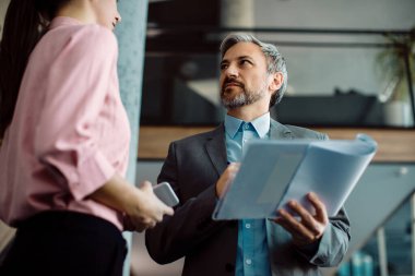 Low angle view of a businessman communicating with female coworker while going through paperwork in a hallway. 