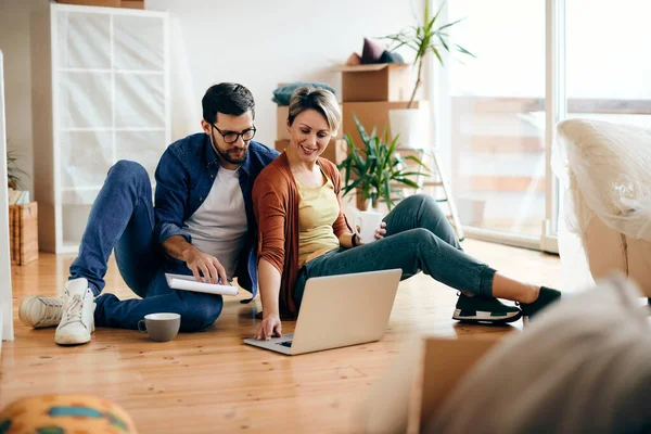 happy couple surfing the net on laptop while sitting on the floor at their new apartment.