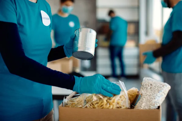 Unrecognizable female volunteer packing food in donation box while working at charity foundation.