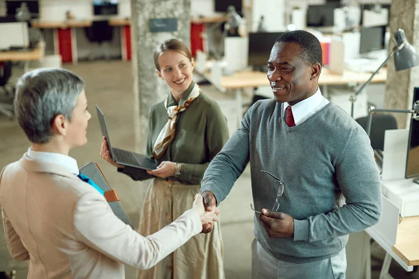 Happy black businessman greeting female corporate manager and shaking hands while welcoming her in the office.