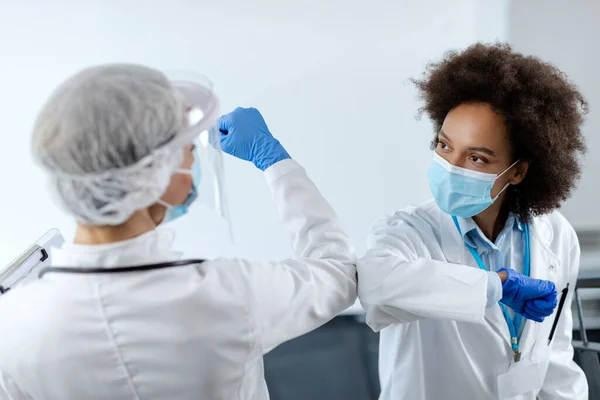 Black female doctor and her colleague greeting with elbows and wearing face masks due to coronavirus pandemic.
