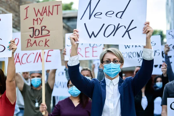 Businesswoman wearing protective face mask and holding banner with Need Work inscription while taking a part in public demonstrations during COVID-19 epidemic.