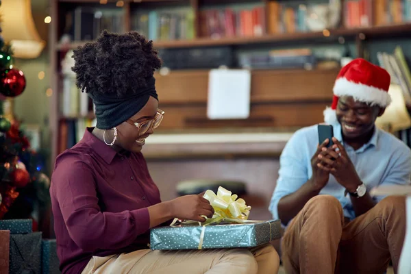 Happy Black Woman Unwrapping Christmas Gift While Her Boyfriend Photographing — ストック写真