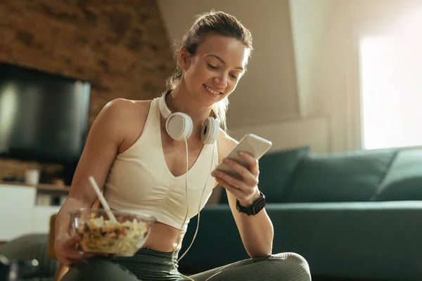 Young Happy Sportswoman Texting Smart Phone While Eating Salad Living —  Fotos de Stock