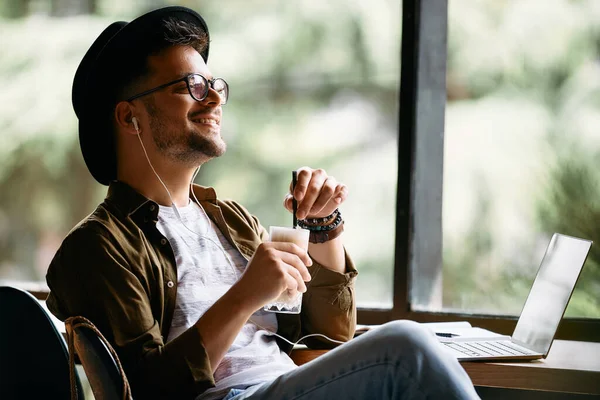 Young happy man drinking coffee and listening music while relaxing after studying in a cafe.