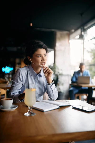 Female entrepreneur making a phone call and communicating via in-ear headphones in a cafe.